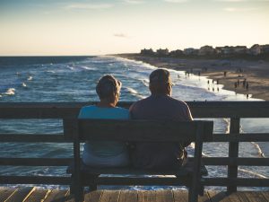 Older couple sitting on a bench looking over the ocean on a pier.