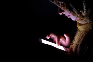A woman wearing a headscarf is focused on her phone, engaged in a conversation or browsing content