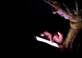 A woman wearing a headscarf is focused on her phone, engaged in a conversation or browsing content