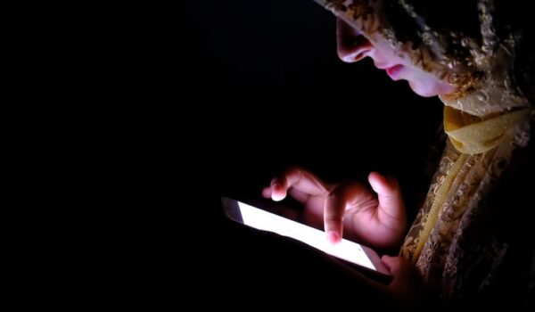A woman wearing a headscarf is focused on her phone, engaged in a conversation or browsing content