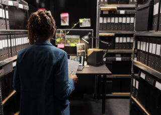 Police investigator holding crime matter file and analyzing evidence board in office late. African american woman law enforcement detective studying clues, working overtime at night