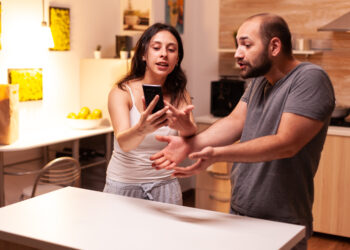 Woman pointing at phone while reading messages of infidel husband while having a disagreement.