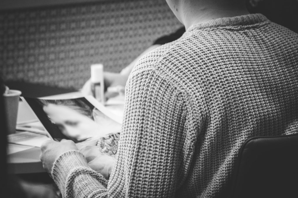 A person in a knitted sweater holds a blurred photograph, examining it closely in a quiet, focused setting