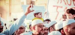 Algerian boy sitting over his father's shoulders in a crowd of people; locate birth parents in Algeria concept