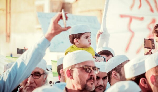 Algerian boy sitting over his father's shoulders in a crowd of people; locate birth parents in Algeria concept