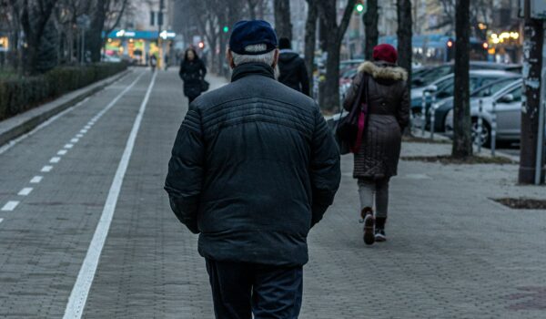 old Bulgarian man walking on a side walk with people walking before him; locate birth parents in Bulgaria concept