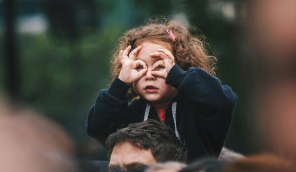 Argentinian girl sitting over her father's shoulders making goggles with her hands; locate birth parents in Argentina