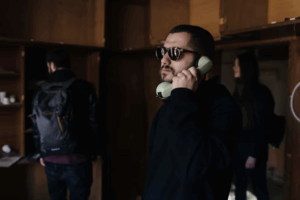 A man wearing sunglasses is talking on a phone while seated in a room