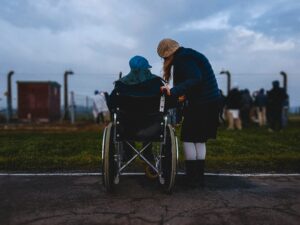 woman standing next to her Polish mother in a wheelchair looking in the horizon; locate birth parents in Poland concept.