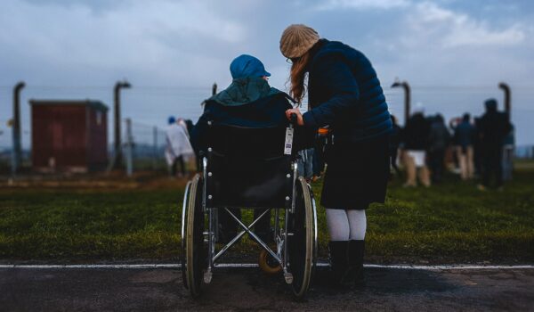 woman standing next to her Polish mother in a wheelchair looking in the horizon; locate birth parents in Poland concept.