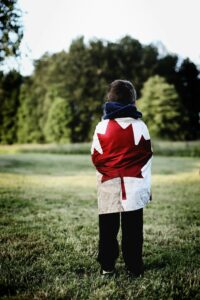 Canadian kid wearing the Canadian flag on his back looking the the forest; locate birth parents in Canada