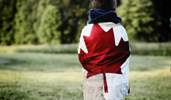 Canadian kid wearing the Canadian flag on his back looking the the forest; locate birth parents in Canada