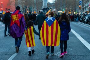 Spanish family of four walking on the street with versions of the Spainish flag on their backs; locate birth parents in Spain concept