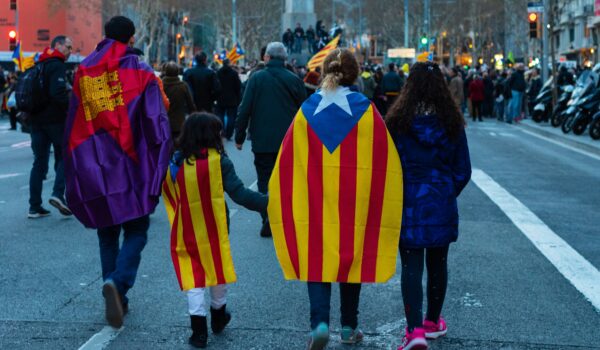 Spanish family of four walking on the street with versions of the Spainish flag on their backs; locate birth parents in Spain concept