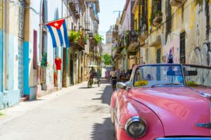 pink car in the streets of Cuba with the Cuban flag; skip tracing services in Cuba concept