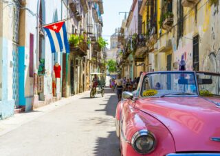 pink car in the streets of Cuba with the Cuban flag; skip tracing services in Cuba concept