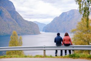 couple sitting on a road barrier looking at the Fjord; locate birth parents in Norway concept