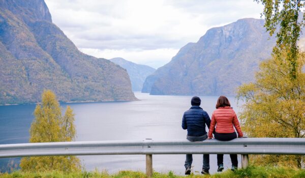 couple sitting on a road barrier looking at the Fjord; locate birth parents in Norway concept