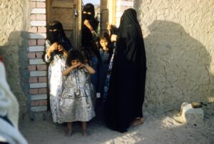 Muslim girls wearing head covers standing outside their gate in Saudi Arabia; locate birth parents in Saudi Arabia concept