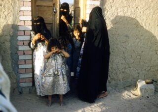 Muslim girls wearing head covers standing outside their gate in Saudi Arabia; locate birth parents in Saudi Arabia concept