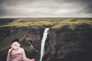 couple looking at Seljalandsfoss Waterfall from a cliff across it; locate birth parents in Iceland concept