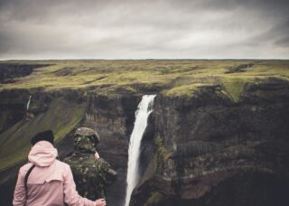 couple looking at Seljalandsfoss Waterfall from a cliff across it; locate birth parents in Iceland concept