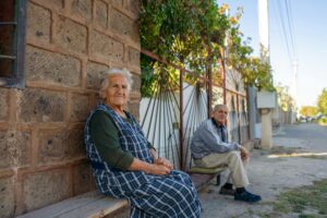 Armenian couple sitting outside their house near the street; locate birth parents in Armenia concept