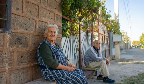 Armenian couple sitting outside their house near the street; locate birth parents in Armenia concept