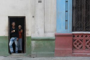 old cuban couple standing at the entrance on their home. locate birth parents in Cuba concept