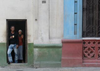 old cuban couple standing at the entrance on their home. locate birth parents in Cuba concept