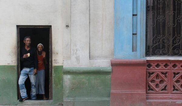 old cuban couple standing at the entrance on their home. locate birth parents in Cuba concept
