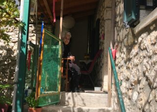 old Greek woman sitting on the porch of her house in Greece; locate birth parents in Greece concept