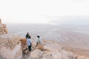 three Israelis sitting on rocks overlooking Masada National Park, Israel; locate birth parents in Israel concept