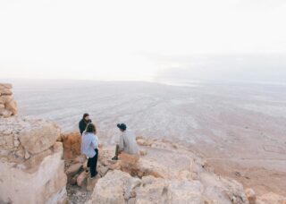 three Israelis sitting on rocks overlooking Masada National Park, Israel; locate birth parents in Israel concept