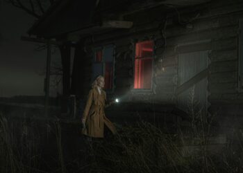 A woman with a flashlight approaches a dark, abandoned house with red-lit windows at night