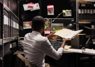 A man sitting at a desk, reading a book with a focused expression